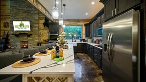 A modern kitchen with a central island, stainless steel appliances, and a stone fireplace. - Runaway Streams - Game Room, Mini Golf, Creekside, EV Outlet (Broken Bow)