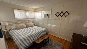 Un dormitorio con cama, mesita de noche, lámpara, ventana, aire acondicionado y una lámpara colgante.
