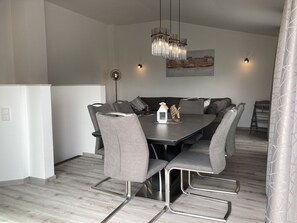 A modern dining area with a rectangular table, grey upholstered chairs, a hanging light fixture, and a cityscape painting on the wall. - "Meeresjuwel" Coralie - "Coralie - Coral" in the house Meeresjuwel! (Dahme)