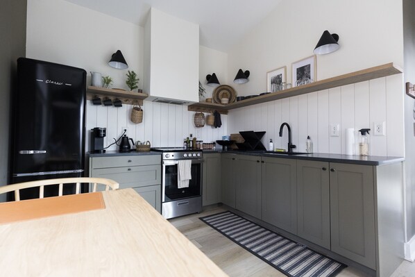 Una cocina moderna con un refrigerador negro, horno de acero inoxidable y una mesa de comedor de madera.