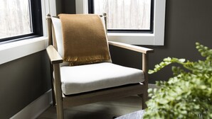 Ein Sessel mit einer braunen Decke, platziert neben einem Fenster mit weißen Vorhängen.