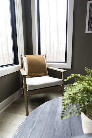 A chair with a brown throw blanket, positioned by a window with white curtains.