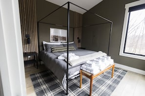 Une chambre à coucher moderne avec un lit à baldaquin, une table de chevet, un banc et une fenêtre donnant sur un beau paysage.