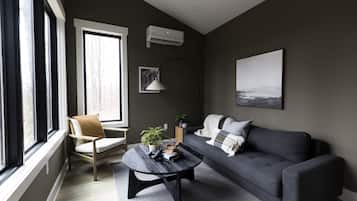 Ein modernes Wohnzimmer mit grauem Sofa, einem runden Couchtisch und einem großen Fenster, das für natürliches Licht sorgt.