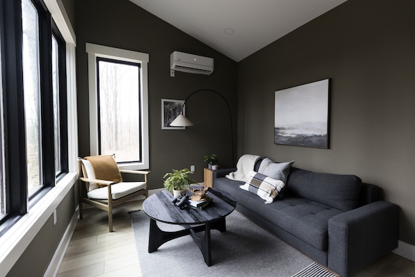 A modern living room with a grey sofa, a round coffee table, and a large window providing natural light.
