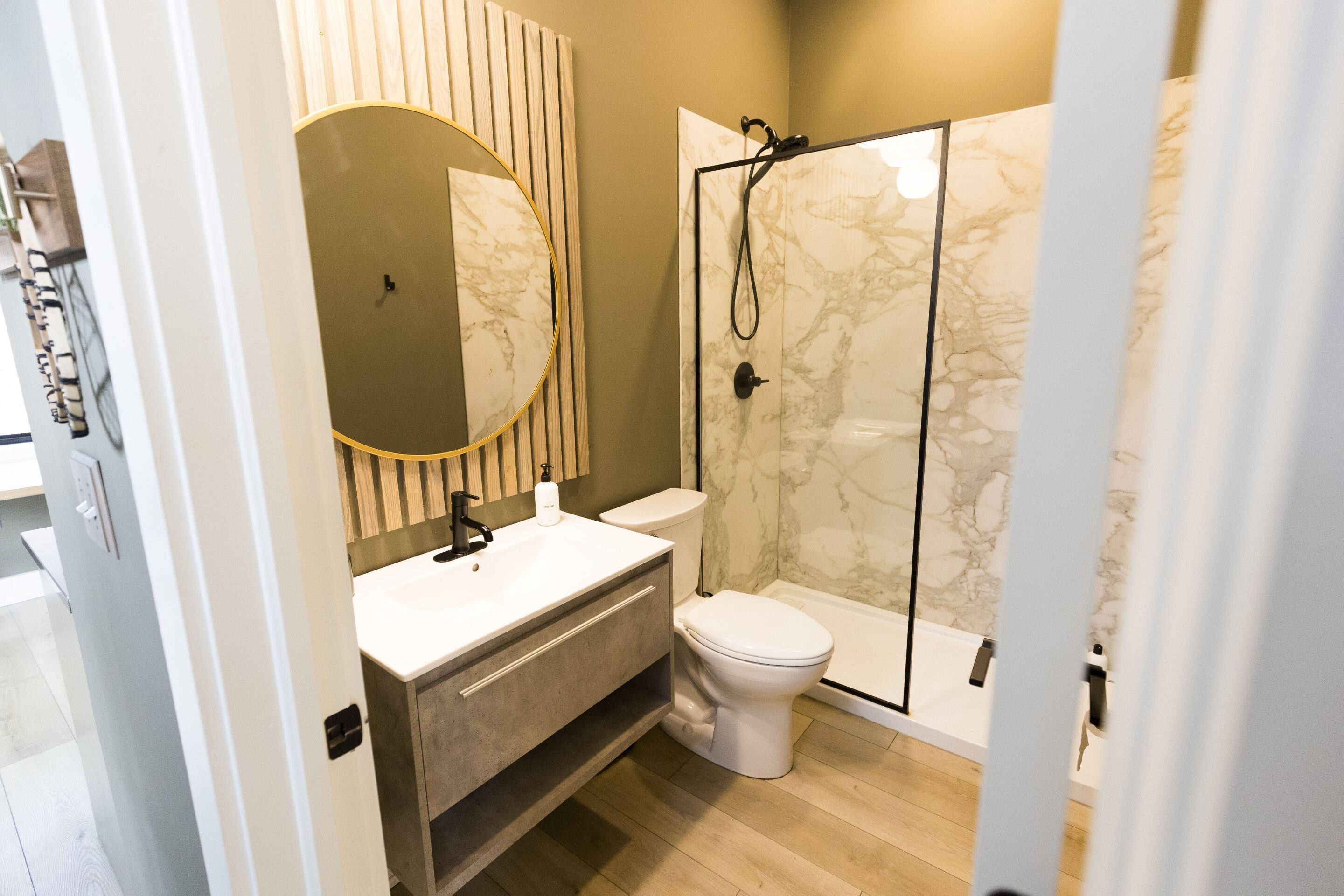 Et moderne badeværelse med en bruseniche i marmor, toilet og en vaskebord-kommode med et stort spejl.
