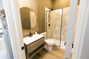Un baño moderno con cabina de ducha de mármol, inodoro y tocador con un espejo grande.