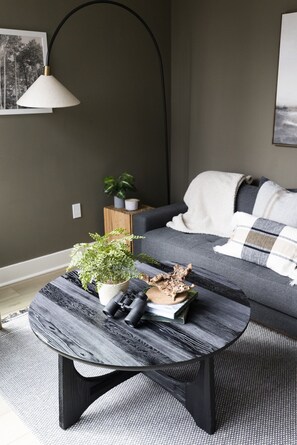 Ein modernes Wohnzimmer mit einem dunkelgrauen Sofa, einem runden Couchtisch mit strukturierter Oberfläche und einer Stehlampe.
