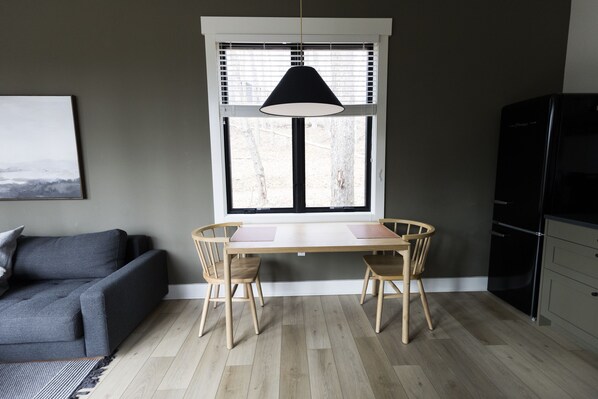A dining area with a table and chairs, a window with blinds, a sofa, and a refrigerator.