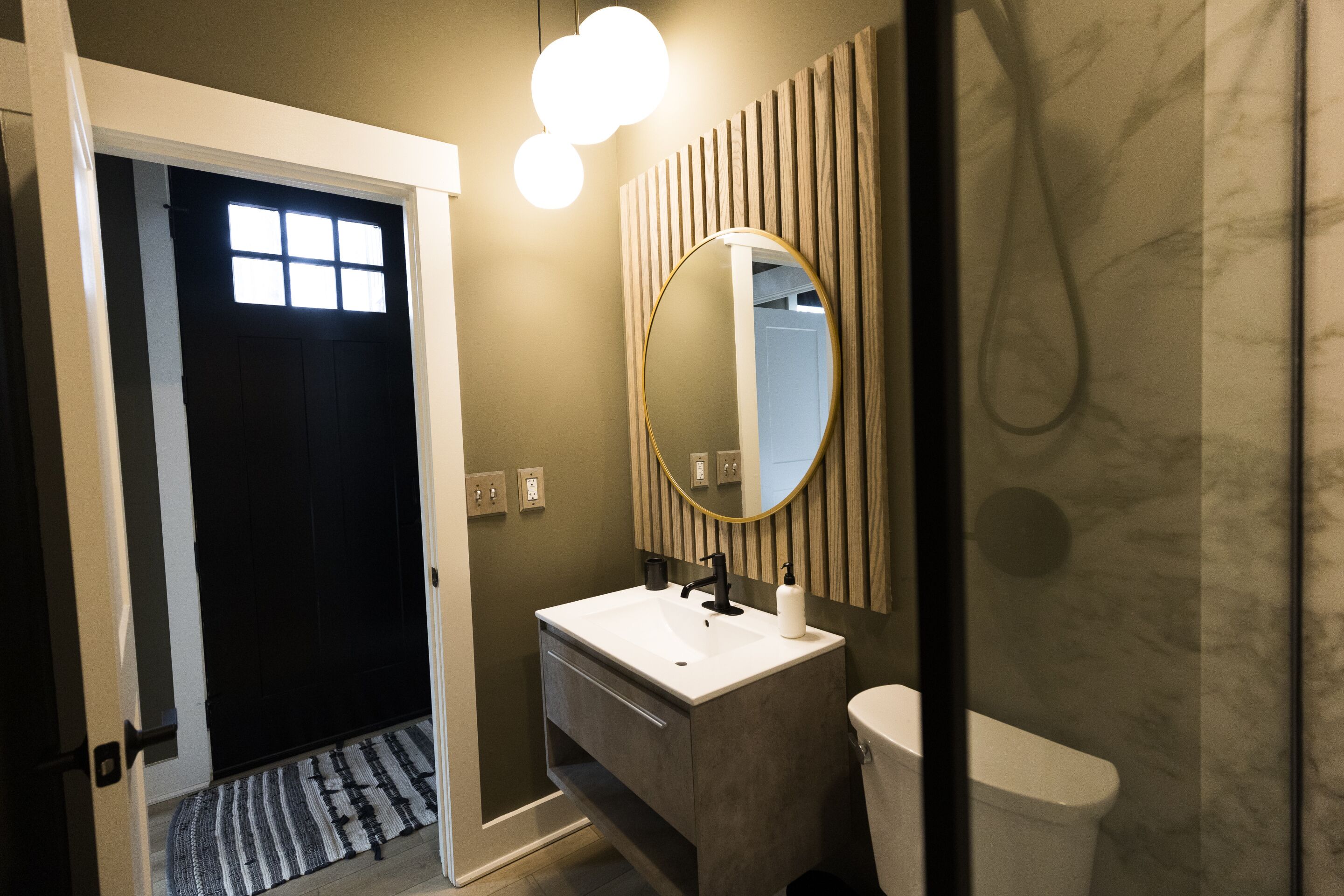 Un baño moderno con un lavamanos blanco, un espejo redondo y un inodoro.