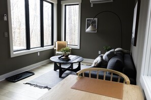 A room with a wooden table, a chair, a sofa, and a small round table with a plant.