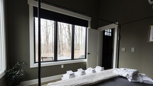 Ein Schlafzimmer mit großem Fenster, einem Bett mit ordentlich gefalteten Handtüchern und einer Zimmerpflanze.