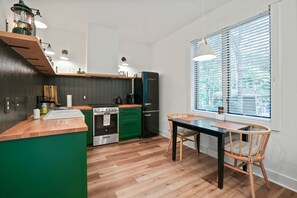 Una cocina moderna con encimera de madera, armarios verdes, refrigerador negro y un comedor con mesa y sillas.
