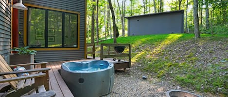 A wooden deck with a hot tub, a wooden chair, and a grill.