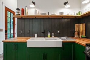 Una cocina con encimera de madera, pileta blanca, armarios verdes y estante de madera sobre la pileta.
