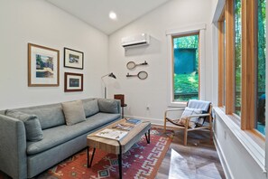 A living room with a grey sofa, a coffee table, a rug, and a window with a view of greenery.