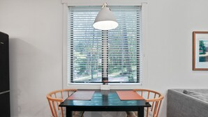 A dining area with a table and chairs, a window with blinds, a hanging light fixture, and a framed picture on the wall.