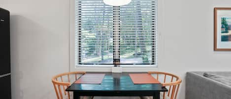 Un área de comedor con una mesa y sillas, una ventana con persianas, un lámpara colgante y un cuadro en la pared.