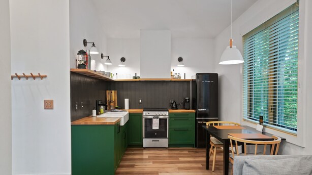 A modern kitchen with green cabinets, a wooden countertop, and a dining area with a table and chairs.