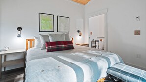 Un dormitorio con cama, mesita de noche, silla, una pequeña mesa y una puerta.
