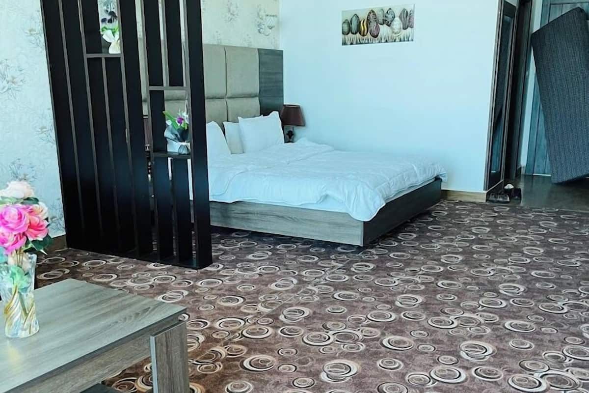 Een slaapkamer met een bed, een nachtkastje, een vaas met bloemen en een kamerbreed tapijt.