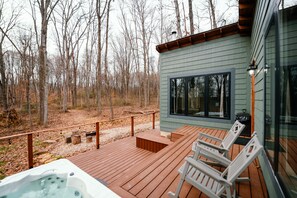 Une terrasse en bois avec un jacuzzi, un coin salon extérieur et une vue sur une forêt.
