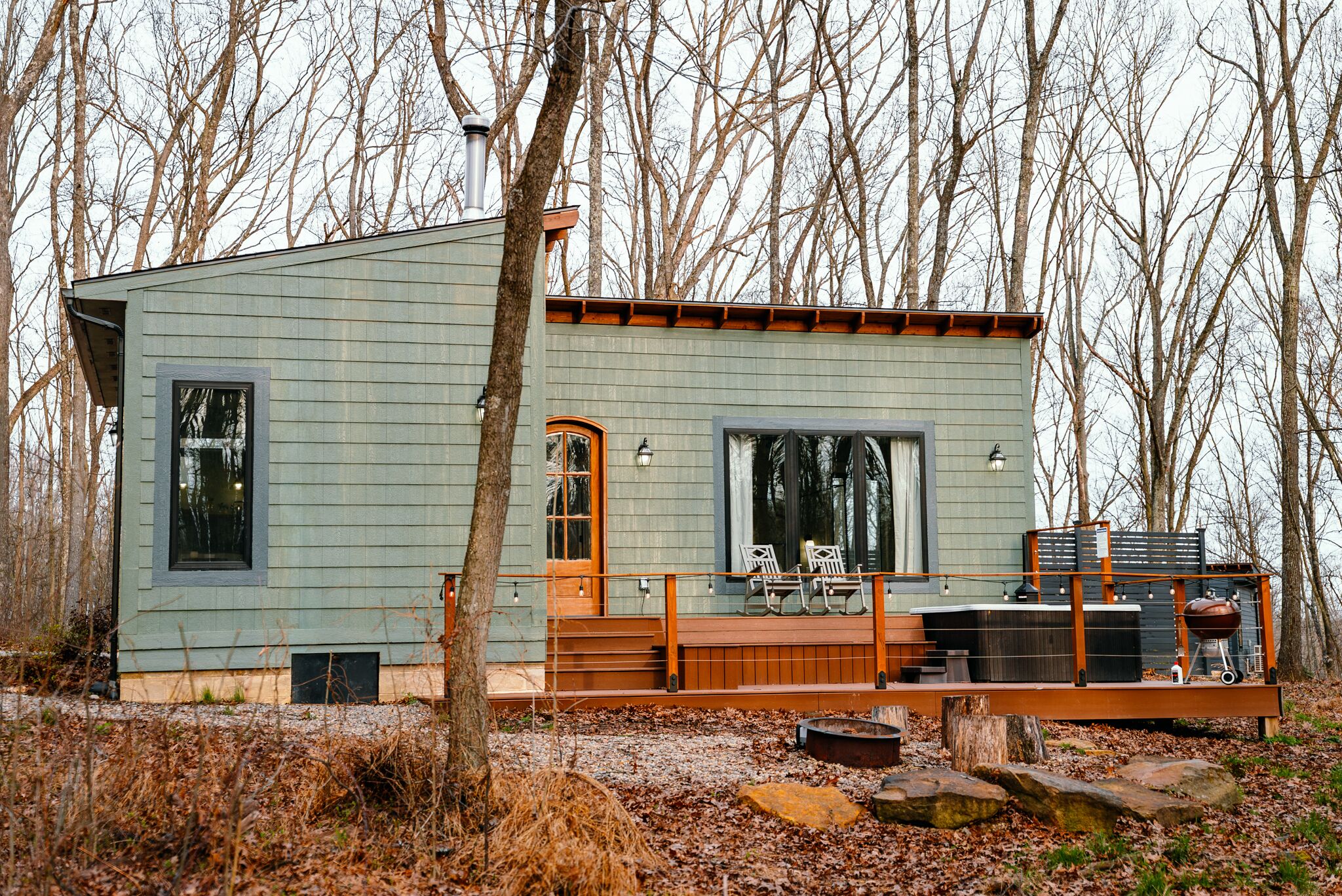 A modern cabin with a deck, large windows, and a fire pit.