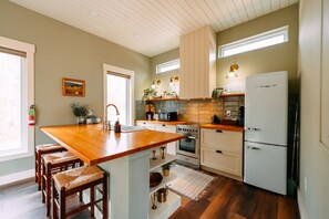 A kitchen with a wooden island, white cabinets, a refrigerator, and a window with a view.