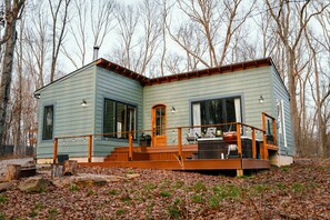 Une cabane à deux étages dotée d’une terrasse, de grandes fenêtres et d’une cheminée.