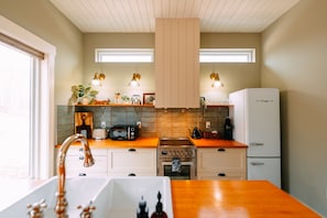 A kitchen with a wooden countertop, a built-in oven, a white refrigerator, and a window above the sink. - Ivy Cottage | Hocking Hills, Modern, Hot Tub (Creola)