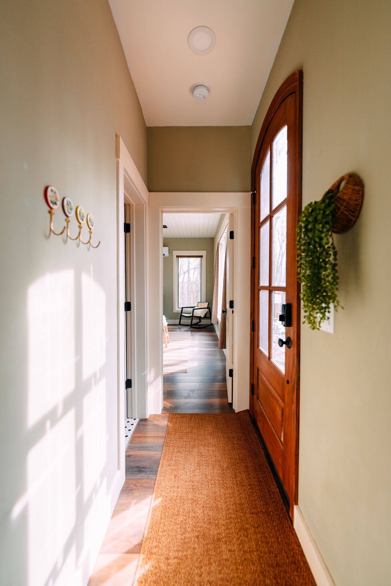 Un pasillo con puerta de madera, planta colgante e iluminación montada en la pared.