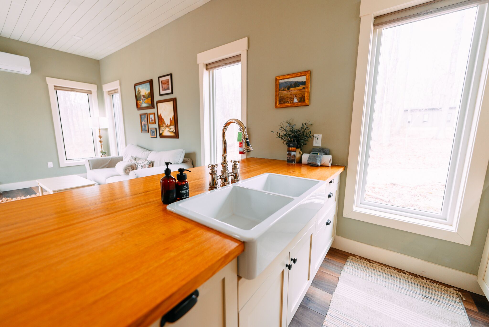 A kitchen with a wooden countertop, white cabinets, a double sink, and a window with a view.
