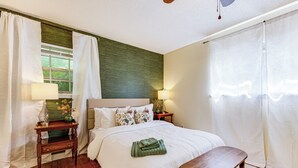 Une chambre à coucher bien aménagée, avec un grand lit, deux tables de chevet avec des lampes, un banc et une vue sur l’extérieur par la fenêtre.