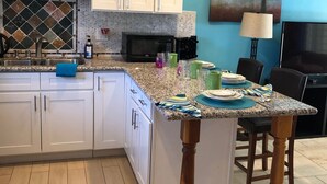 A kitchen with white cabinets, a granite countertop, a microwave, and a dining area with a table and chairs. - Quaint apartment with AC in lovely Oceanside (Oceanside)