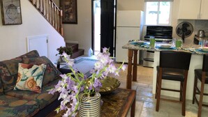 A living room with a sofa, a coffee table with a vase of flowers, a staircase, a kitchen area with a refrigerator, stove, and dining table with chairs. - Quaint apartment with AC in lovely Oceanside (Oceanside)