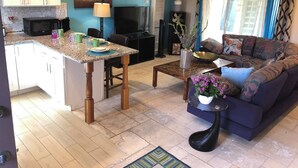 A modern kitchen with a central island, a dining area with a sofa, and a living room with a ceiling fan. - Quaint apartment with AC in lovely Oceanside (Oceanside)