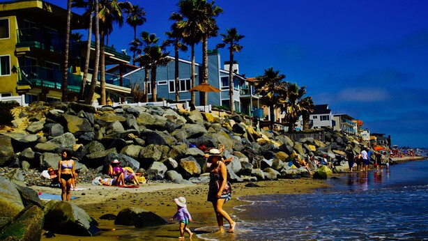 A beach with rocky terrain, palm trees, and buildings along the shore. - Quaint apartment with AC in lovely Oceanside (Oceanside)