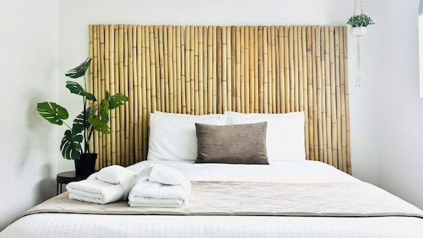 A neatly made bed with white linens, a bamboo headboard, and a potted plant beside it.