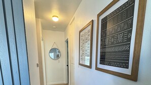 A hallway with wooden flooring, white walls, and two framed wall art pieces.