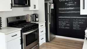 A modern kitchen with white cabinets, stainless steel appliances, and a chalkboard wall listing top 5 attractions in California.