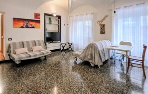 A furnished room with a sofa, a covered chair, a table, and a television.