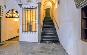 A stone staircase leading to a door with a barred window, a wall with a decorative arch, and a light fixture.