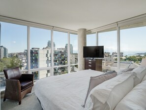 A modern hotel room with a large bed, a TV, and a city view. - Harbour Vista - Breathtaking Views, Workspace, Gym, and Nearby Shopping Nearby by Victoria Prime!! (Victoria)