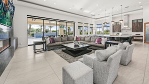 A spacious living area with a large sectional sofa, a coffee table, and a fireplace. - Palm Villa- Luxury 8 Bed, Pickleball, Volleyball, Golf (Bermuda Dunes)