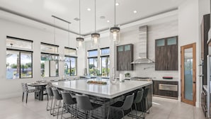 A spacious kitchen with a large island, modern pendant lights, and a view of the outdoors. - Palm Villa- Luxury 8 Bed, Pickleball, Volleyball, Golf (Bermuda Dunes)