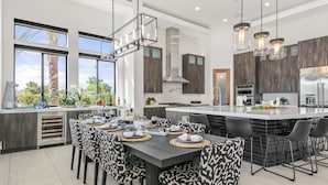A modern kitchen with a central island, dining area with patterned chairs, and large windows with a view. - Palm Villa- Luxury 8 Bed, Pickleball, Volleyball, Golf (Bermuda Dunes)