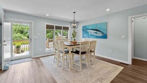 A dining area with a table and chairs, a chandelier, and a painting of a shark on the wall. - Salty Bunker | 5200 ft to the beach | Private Pool (Kitty Hawk)