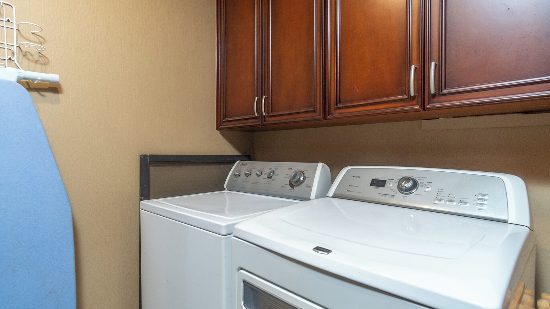 A laundry area with two white washers and dryers, wooden cabinets above, and a blue towel rack.