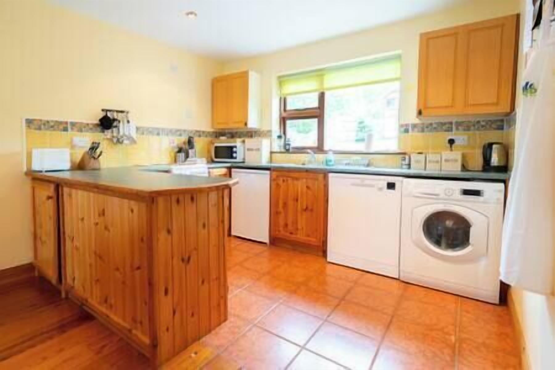 A kitchen with wooden cabinets, a microwave, a washing machine, and a sink.