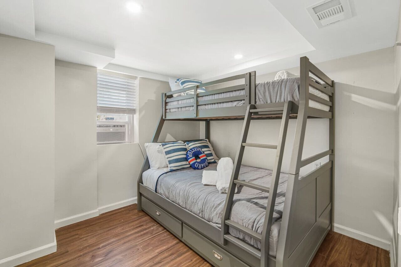 A bunk bed room with a window, wooden flooring, and a ceiling vent.